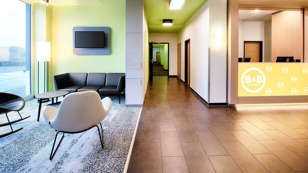 Een hotel receptie met een receptiebalie, een zithoek en een aan de muur bevestigde televisie.
