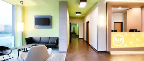 Zona de recepción de hotel con mostrador, asientos y un televisor en la pared.