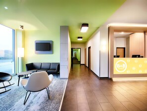 Ein Hotel-Empfangsbereich mit Empfangstresen, Sitzgelegenheiten und einem an der Wand befestigten Fernseher.