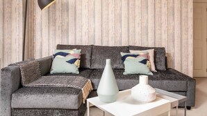 Un salon avec un canapé gris, un plaid à motifs, une table basse blanche et un lampadaire noir.