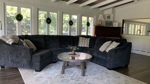 Un salon avec un canapé d’angle gris foncé, une table basse ronde en bois et un tapis à motifs.