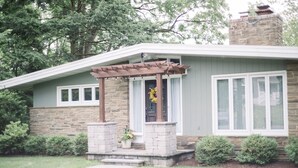 Une maison avec une façade en pierre, un porche couvert agrémenté d’une pergola et une porte d’entrée ornée d’une guirlande.