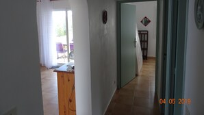 A hallway with a wooden cabinet, a door, and a view of an outdoor area with chairs and a table. - Detached villa 4/6 persons 3 terraces - Palombaggia magnificent sea view (Porto-Vecchio)