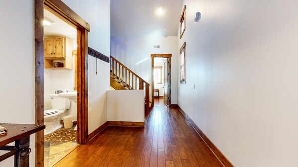 A hallway with wooden flooring, a staircase, and a view into a room with a toilet and cabinets. - One of a Kind, Pet-Friendly, Beautiful & Spacious, Washer/Dryer, 1-Car Garage (Mammoth Lakes)
