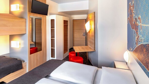 A modern hotel room with a bed, a desk, a red chair, and a TV. - B&B Hotel Magdeburg-City (Magdeburg)