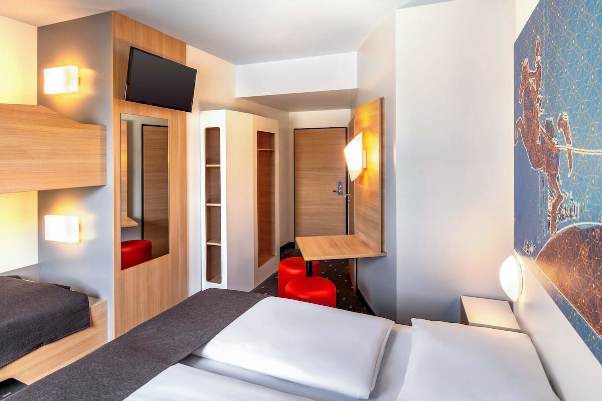 Ein modernes Hotelzimmer mit einem Bett, einem Schreibtisch, einem roten Sessel und einem Fernseher.