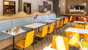 A modern restaurant with long communal tables and booths, featuring vibrant yellow chairs and a mix of seating arrangements. - B&B Hotel Magdeburg-City (Magdeburg)