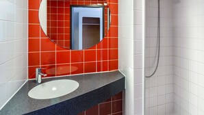 A bathroom with a white sink, a round mirror, and a shower. - B&B Hotel Magdeburg-City (Magdeburg)