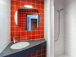 Ein Badezimmer mit einem weißen Waschbecken, einem runden Spiegel und einer Dusche.