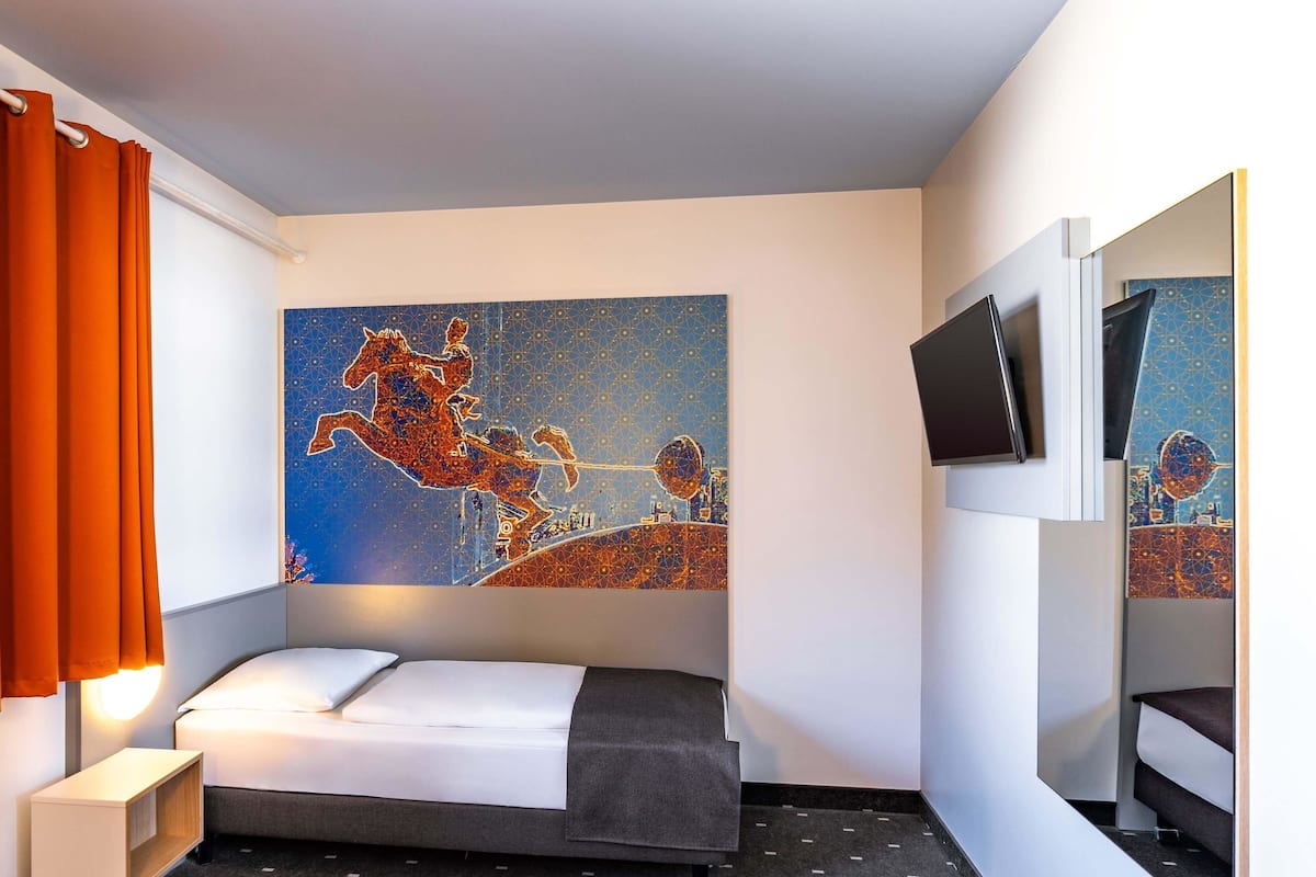 Ein Hotelzimmer mit einem Bett, einem Fernseher, einem Gemälde und orangenen Vorhängen.