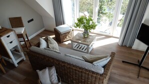 Una sala de estar acogedora con un sofá de mimbre, una mesita con una planta y un mueble para televisión.