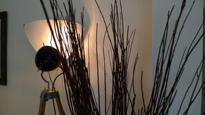 A lamp with a white shade and a dark base on a tripod stand, surrounded by bare branches against a wall. - Hotel Leegerpark (Krummhoern)