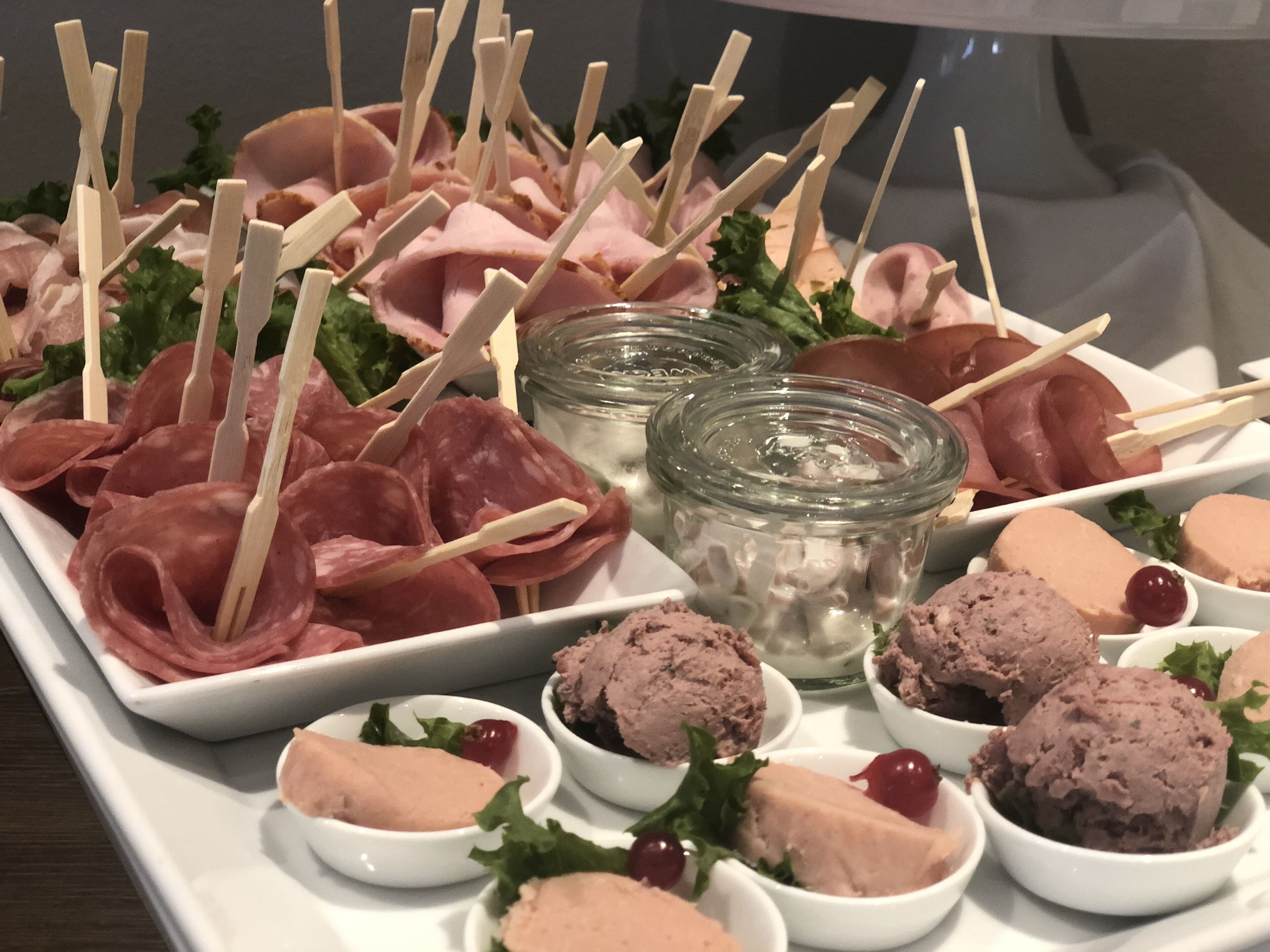 Eine Platte mit verschiedenen Fleischsorten und Pasteten, bestückt mit Zahnstochern, garniert mit Kräutern und Kirschen.