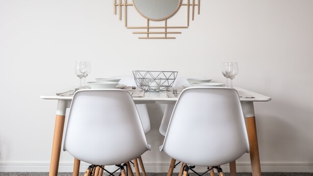 Une table à manger avec deux chaises blanches, un miroir rond et un élément de décoration murale aux motifs géométriques.