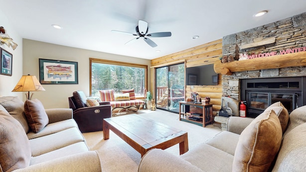 A cozy living room with a fireplace, comfortable seating, and a large window overlooking a forest. - Remodeled Cabin, Balcony. Near Walking Trails. Pool & Tennis Courts On-site (Mammoth Lakes)
