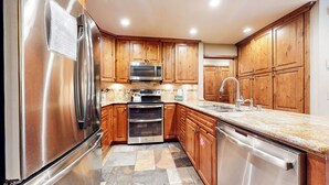A kitchen with wooden cabinets, stainless steel appliances, a granite countertop, and a tiled backsplash. - Remodeled Cabin, Balcony. Near Walking Trails. Pool & Tennis Courts On-site (Mammoth Lakes)