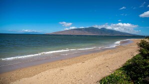 A beach with a mountain in the background, clear skies, and calm waters. - Oceanfront Penthouse Vistas (Kihei)