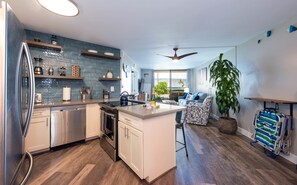Une cuisine moderne dotée d’un îlot central, d’appareils électroménagers en acier inoxydable et offrant une vue sur l’extérieur.