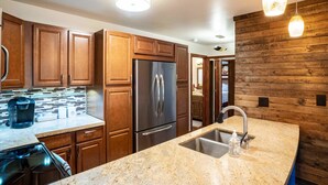 Una cocina con armarios de madera, un refrigerador de acero inoxidable, una encimera de granito y una lámpara moderna.