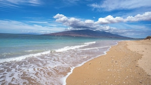 Une plage à l’eau claire, un rivage sablonneux et une montagne qui se profile à l’horizon.