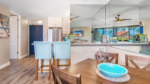 Une cuisine moderne avec un coin repas, des chaises en bois, un saladier bleu sur la table et un ventilateur de plafond.