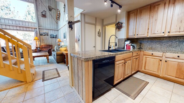 Kitchen features a dishwasher, sink, and island, with a staircase leading to an upper level and a seating area.