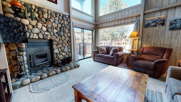 A cozy living room with a stone fireplace, comfortable seating, and a large window offering a view of the outdoors.