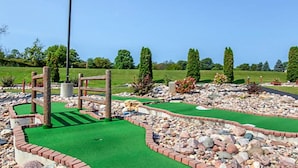 Un campo de mini golf con una superficie de césped verde, un puente de madera y un asta con bandera roja.