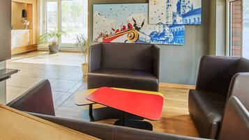 A modern lobby with leather seating, a red and yellow table, and artwork depicting a cityscape and a boat.