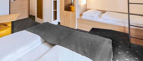 A hotel room with a bunk bed, a desk, a chair, a TV, and built-in shelving.