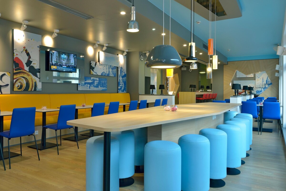 Ein modernes Restaurant mit hohen Tischen, blauen Stühlen und einer langen Theke.