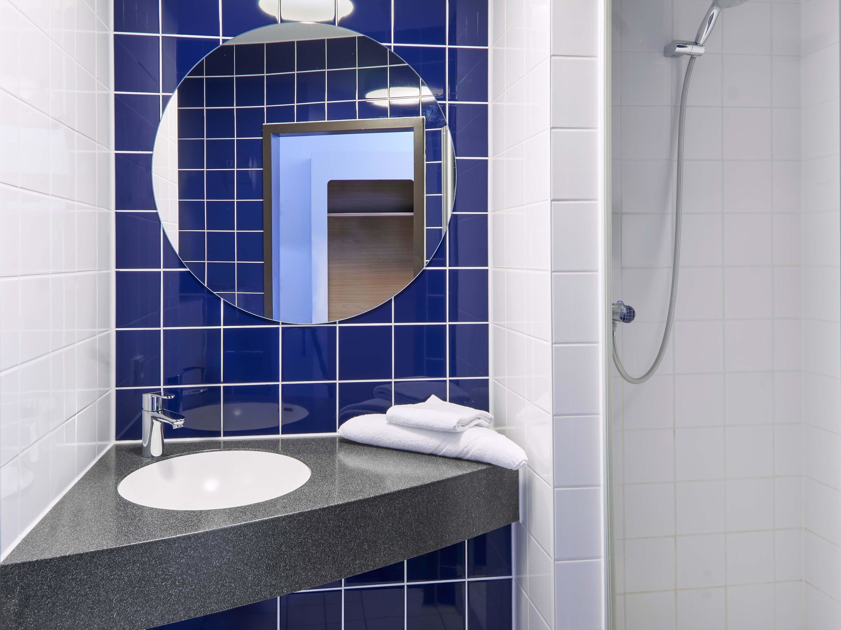 Ein Badezimmer mit rundem Spiegel, Waschbecken und Dusche.