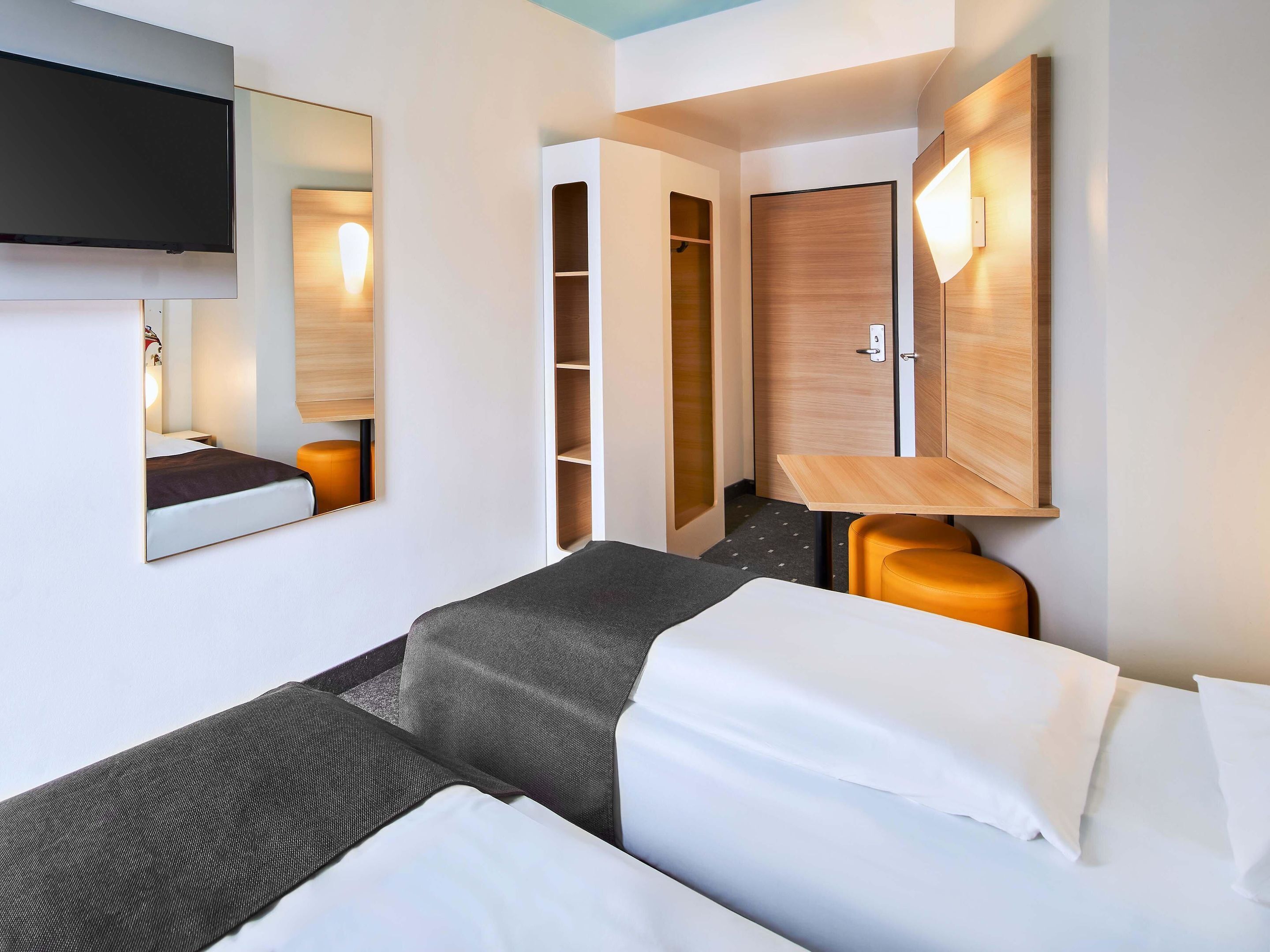 Habitación de hotel con cama, escritorio, armario y televisor montado en la pared.