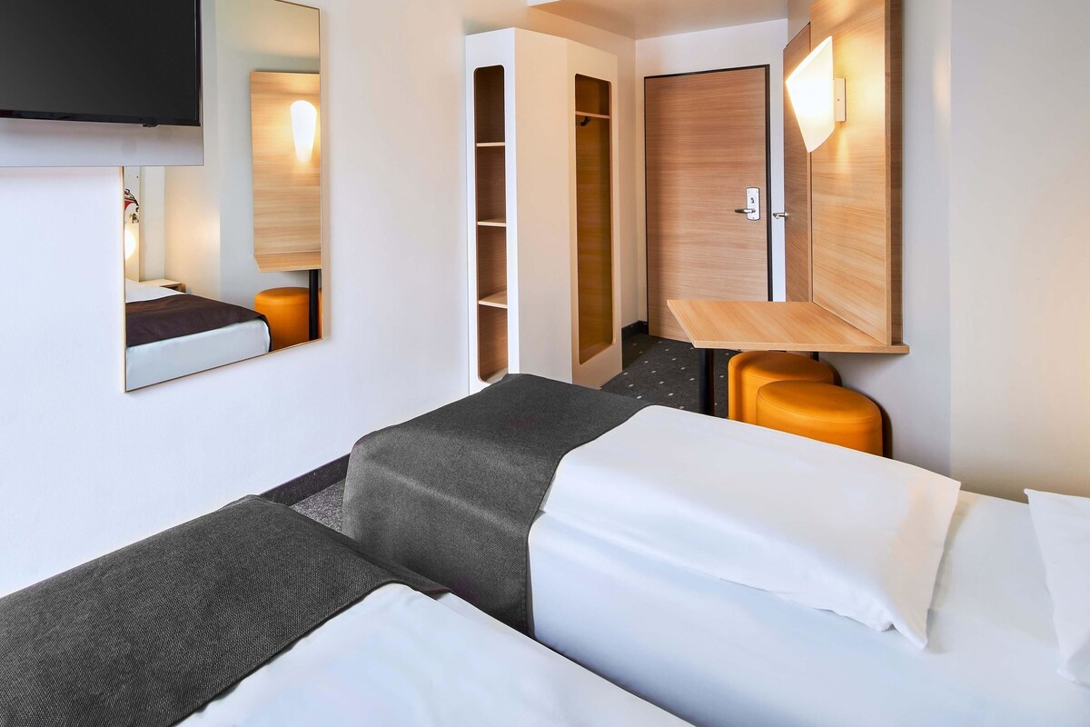 Une chambre d’hôtel équipée d’un lit, d’un bureau, d’une armoire et d’un téléviseur fixé au mur.