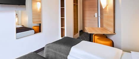 Habitación de hotel con cama, escritorio, armario y televisor montado en la pared.