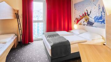 A hotel room with a bunk bed, a desk, a chair, a window with red curtains, and a cityscape view.