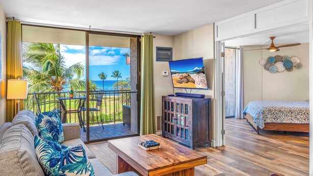 A room with a balcony, a bed, a TV, and a coffee table. - Refined Oceanfront Vistas (Kihei)