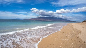A beach with clear water, a sandy shore, and a mountain in the distance. - Refined Oceanfront Vistas (Kihei)