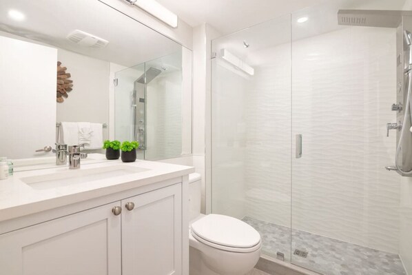 A modern bathroom with a glass-enclosed shower, a white sink, and a toilet.