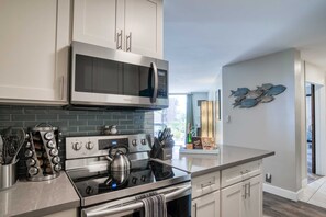 A modern kitchen with stainless steel appliances, white cabinetry, and a decorative fish wall art piece.