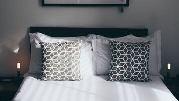A neatly made bed with white linens and patterned pillows, a framed picture above it, and two bedside lamps.