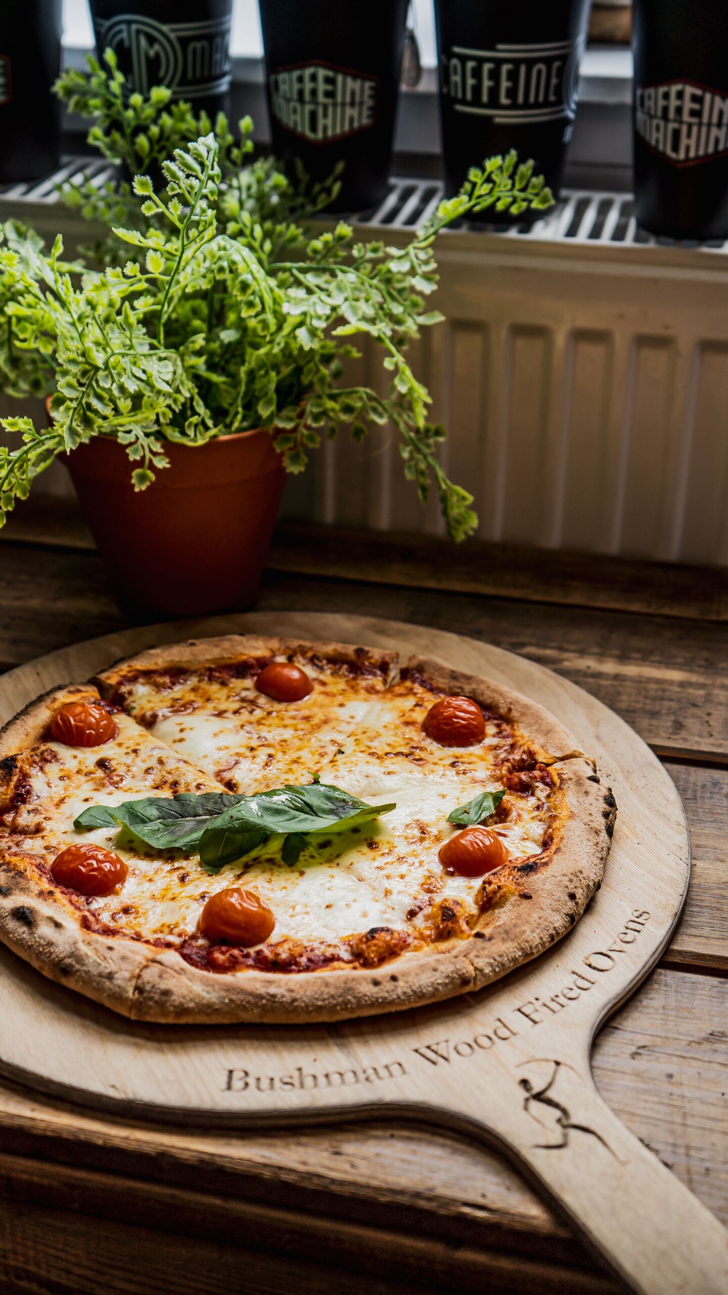 A pizza on a wooden board with "Bushman Wood Fired Ovens" written on it.