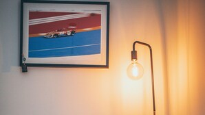 Ett sovrum med en säng, en inramad tavla på väggen och en golvlampa.