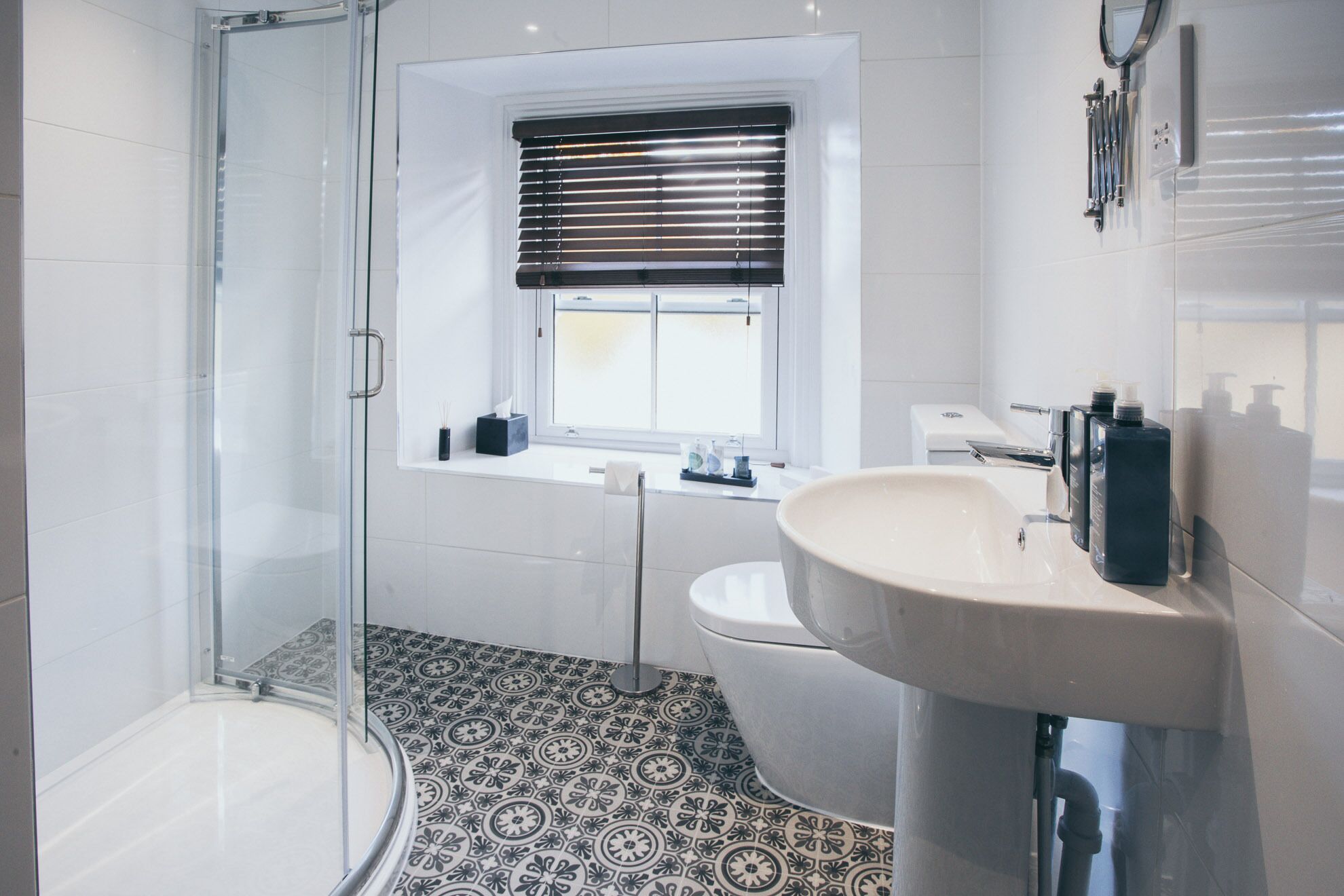 Une salle de bain moderne avec une douche à parois de verre, des toilettes, un lavabo avec un miroir et une fenêtre équipée de stores.