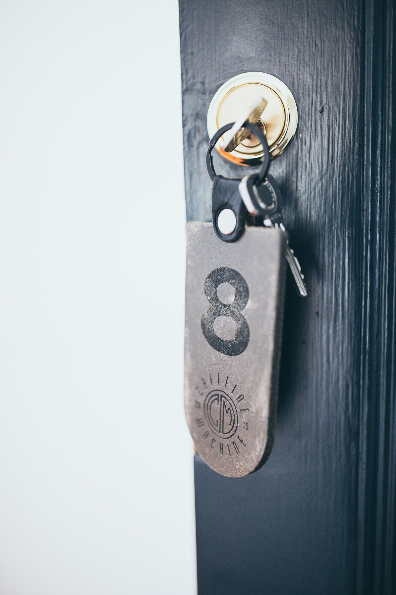 A metallic keychain with a number 8 and a logo, attached to a keyring, hanging on a door.