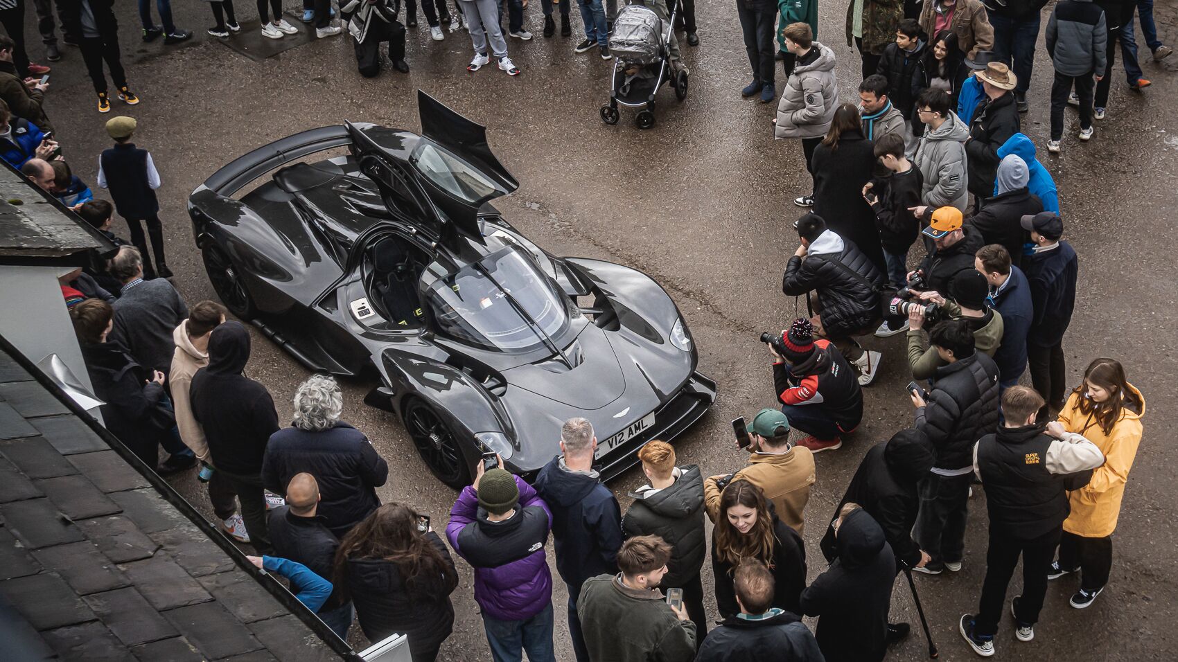Een menigte mensen verzameld rond een zwarte sportauto.