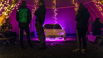 Una carpa con gente de pie alrededor de un coche con luces moradas.