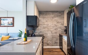 Une cuisine moderne dotée d’un îlot central intégré, d’appareils électroménagers en acier inoxydable et d’un dosseret orné d’un motif en chevrons.