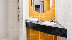 Une salle de bain avec un lavabo blanc, un plan de toilette noir et un miroir doté d’un cadre rond.