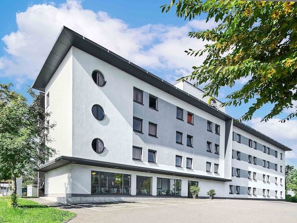 Ein modernes Mehrstöckhotel mit weißer Fassade, großen Fenstern und einem Flachdach.